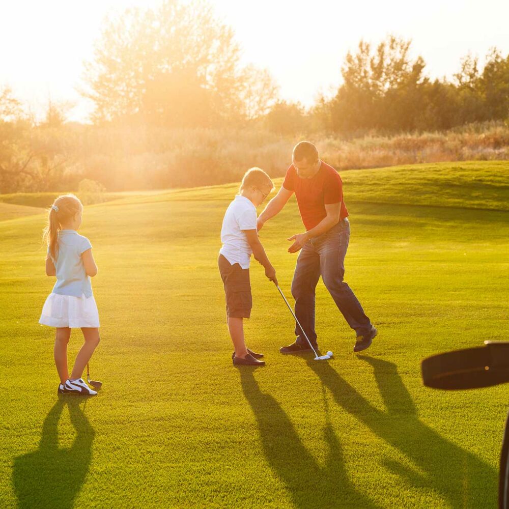 Kinder auf einem Golfplatz, die Golfschläger in der Hand halten und mit einem Trainer